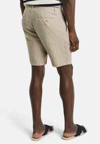 Beige gestreepte shorts van lichtgewicht stof, met een achterzak en een relaxte pasvorm, gecombineerd met marineblauwe sandalen.