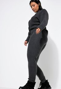 Grauer Strickpullover und passende Hose aus weichem Stoff, mit lockerer Passform, gerippten Bündchen und elastischem Bund mit Kordelzug. Klobige schwarze Stiefel.