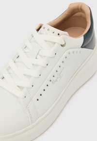 Balts ādas sporta apavu ar apaļu purngalu, auklas aizdari, sudrabkrāsas kniedēm un tumši zaļiem akcentiem papēdī. Iekšpuse ar bēša krāsas polsterējumu.