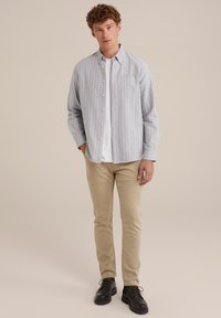 Randig skjorta i ljusblått med tunna vita och orangea ränder, med en bröstficka. Åtföljs av beige byxor och svarta skor.