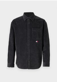 Camicia in corduroy grigio scuro con maniche lunghe, chiusura con bottoni e tasca sul petto. Presenta una piccola etichetta con logo in rosso, bianco e blu.