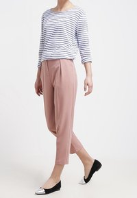 Gestreiftes, langärmliges Oberteil in Weiß und Marineblau, kombiniert mit rosa Hosen. Schwarze Ballerinas mit metallischen Spitzen vervollständigen das lässige Outfit.