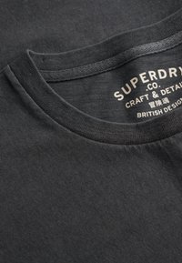 Ciemnoszara koszulka T-shirt z okrągłym dekoltem. Miękka, prążkowana tekstura ze szczegółami przeszycia. Etykieta marki widoczna wewnątrz kołnierza.