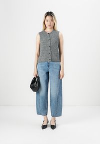 Top grigio lavorato a maglia senza maniche con bottoni frontali, abbinato a jeans a vita alta blu chiaro a gamba larga e tacchi a punta neri. Borsa nera.