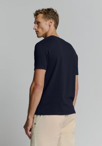 Navyblauw T-shirt met korte mouwen en een gestructureerd ribbelpatroon, ronde halslijn en een relaxte pasvorm, gecombineerd met lichtbeige broeken.