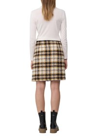 Beige en bruine geruite rok van stevig weefsel, gecombineerd met een witte blouse met lange mouwen en zwarte enkelboots.