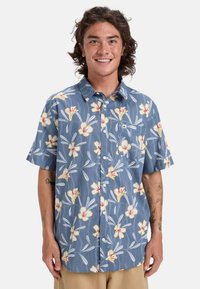 Košile na knoflíky s krátkým rukávem v modré barvě s bílým a žlutým květinovým vzorem. Obsahuje kapsu a lehkou texturovanou tkaninu.