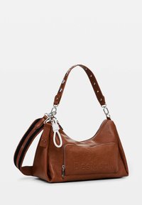 Braune Lederhandtasche mit einem lässigen Design und einer vorderen Reißverschlusstasche. Verfügt über einen dekorativen Riemen mit Nieten und einer silbernen Metalkette.