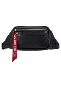 Musta nahkainen vyölaukku, jossa on etuvetoketju, kohokuvioitu teksti "POISTA ENNEN LENTOA" ja punainen kangastarra, jossa on valkoiset kirjaimet.