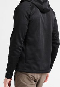 Zwarte hoodie van een gestructureerde stof, met een getailleerd ontwerp en een gebogen zoom. De achterkant toont zichtbare naden en een gladde afwerking.