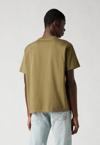 Olive green cotton T-shirt with a relaxed fit, short sleeves, and a round neckline, paired with light blue denim jeans.