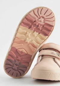 Chaussure rose pâle avec des bandes Velcro ; semelle en caoutchouc texturée dans des dégradés de rose et de beige avec des motifs d'étoiles et une étiquette de taille « 6 ». 