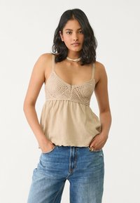 Haut cropped beige avec des détails en crochet délicat et des bretelles ajustables, associé à un jean bleu taille haute. Tissu texturé avec un ourlet volanté.