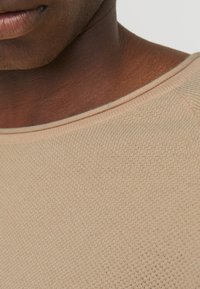 Beżowy sweter dziany z teksturowanej, oddychającej tkaniny, z szerokim dekoltem i subtelnymi detalami szwów wzdłuż brzegów.