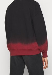 Felpa nera e bordeaux con un effetto ombré gradient, caratterizzata da una vestibilità morbida e polsini a costine, realizzata in tessuto morbido.