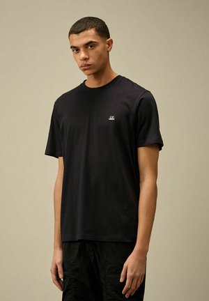 T-shirt in cotone nero con maniche corte, colletto rotondo e piccolo logo sul petto. Tessuto liscio, vestibilità comoda, abbinato a pantaloni corti scuri.