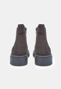 Bocanci scurți din suede maro, cu o textură netedă, talpă plată din cauciuc negru și fermoare laterale pentru a fi ușor de purtat. Design simplu și modern.