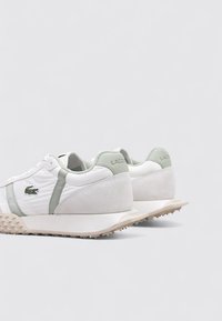 Zapatillas blancas con acentos en verde claro, que combinan materiales de cuero liso y ante, suela texturizada y el logo de Lacoste en el lateral.