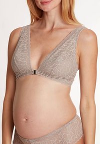 Blonde amme-bh i lys beige med dyb V-udskæring, brede stropper og en sølvfarvet lukning foran. Har et tekstureret bladmønster over det hele.