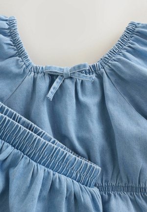Světlé modré džínové oblečení s nařaseným výstřihem s detailem mašle a elastickým pasem pro pružné nošení. Hladká textura.