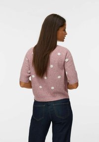 Maglione rosa a maniche corte con pois bianchi, in materiale a maglia texture, design aderente e orlo a costine, abbinato a jeans scuri.