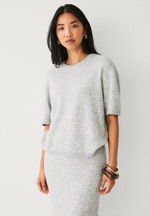 Grey knit sweater with short sleeves, round neckline, textured finish, paired with a matching skirt. Features bracelets on the wrist.