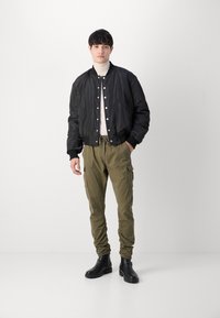 Zwarte bomberjack met geribbelde manchetten, beige coltrui, olijfgroene cargobroek en zwarte enkellaarsjes; slim fit, praktische zakken op de broek.