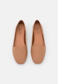Ballerines en cuir tan avec un bout rond, texture lisse et semelle intérieure rembourrée. Marque visible à l'intérieur sur la semelle.