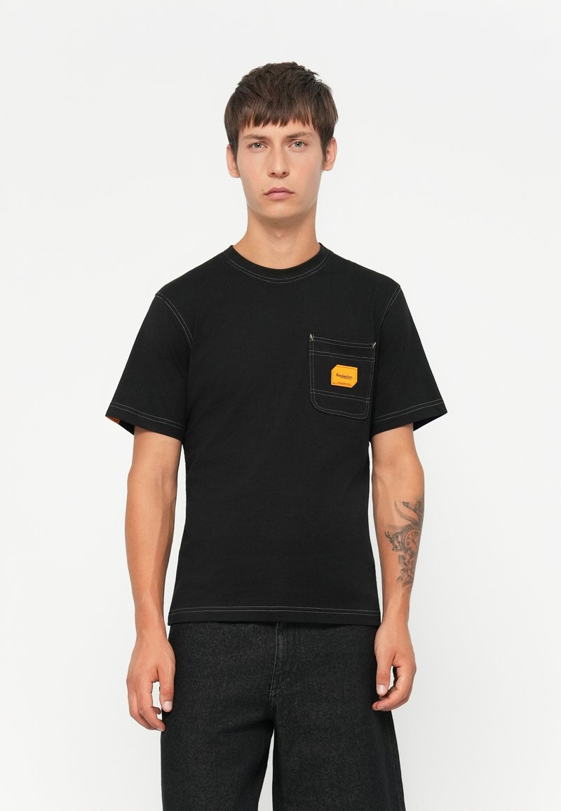 Μαύρο βαμβακερό T-shirt με κοντά μανίκια και τσέπη στο στήθος. Διαθέτει λευκή ραφή και κίτρινο ορθογώνιο λογότυπο στην τσέπη.