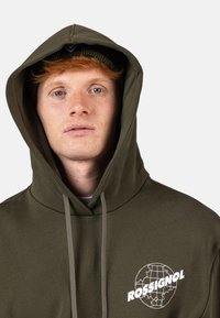 Felpa con cappuccio verde oliva con coulisse, tessuto morbido e logo bianco con un design a forma di globo. Accompagnata da un berretto di maglia coordinato.