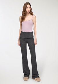 Jasnoróżowy body na cienkich ramiączkach w połączeniu z ciemnoszarymi spodniami o szerokich nogawkach z miękkim, złożonym paskiem w talii. Miękka tekstura, casualowy design.