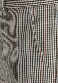 Gros plan sur un tissu rayé beige, noir, bleu et rouge avec des lignes diagonales et verticales formant un motif tissé texturé.