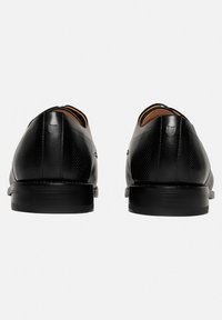 Chaussures en cuir noir avec une finition lisse et un design perforé sur les côtés. Bout rond et talon bas en caoutchouc texturé pour plus de stabilité.