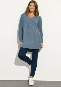 Hellblauer Strickpullover mit V-Ausschnitt und Zopfmuster, kombiniert mit dunkelblauen Skinny Jeans und weißen Sneakers.