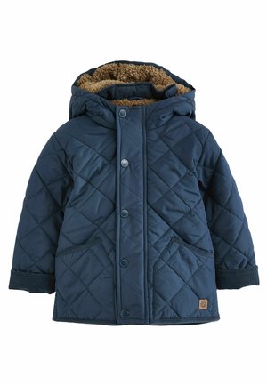 Veste matelassée bleu marine avec capuche, doublée de fausse fourrure, boutons-pression, deux poches avant et poignets contrastants. Forme rectangulaire.
