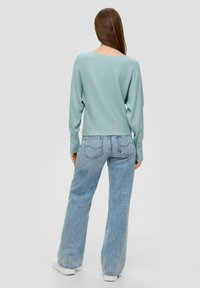 Hellblauer gerippter Pullover mit rundem Rückenausschnitt, kombiniert mit hochgeschnittenen, ausgebleichten blauen Jeans und weißen Sneakers.