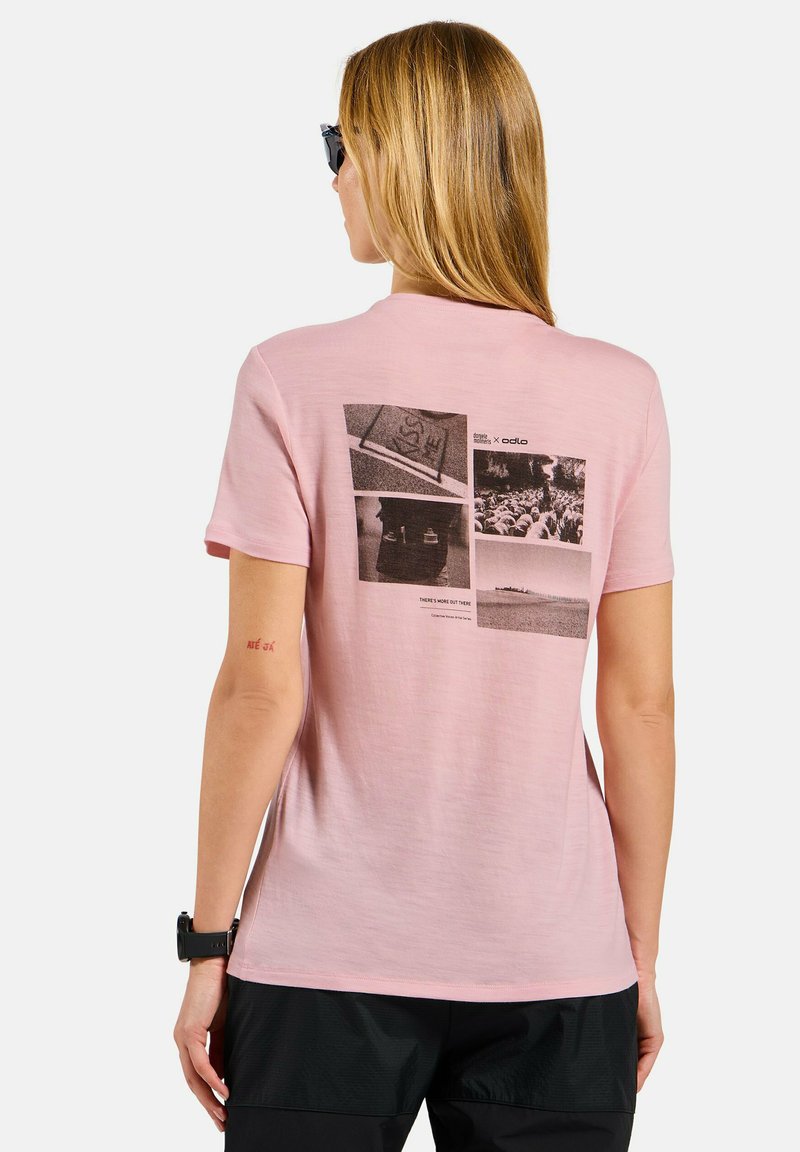 Frau mit langen blonden Haaren, die eine Sonnenbrille trägt, ein pinkes T-Shirt mit schwarzen und weißen Fotodrucken auf der Rückseite und schwarze Shorts.