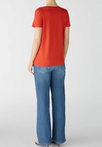 Rode T-shirt met korte mouwen en een ronde hals, gecombineerd met lichtblauwe flared jeans. Glad textuur en casual pasvorm. Schoeisel niet zichtbaar.