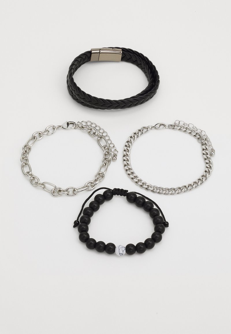 Quatre bracelets : un bracelet en cuir tressé noir, deux bracelets chaîne en argent, et un bracelet en perles noires avec une perle d'accent blanche, tous exposés sur un fond blanc.