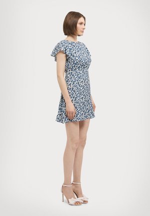 Bloemige jurk in wit en blauw; korte gerimpelde mouwen, aansluitende lijfje, uitlopende rok, gecombineerd met lichtroze hakken.