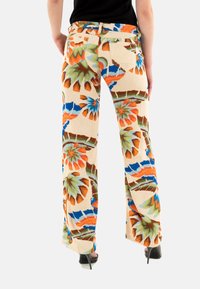 Pantalons évasés en tissu beige clair avec des motifs floraux vibrants en orange, vert et bleu. Comprend des poches arrière et une taille mi-haute.