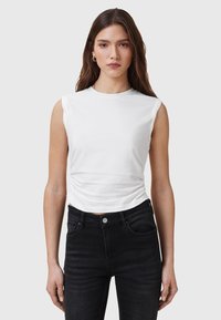 Top bianco senza maniche con scollo rotondo, caratterizzato da leggere pieghe sui lati. Abbinato a jeans neri a vita alta.