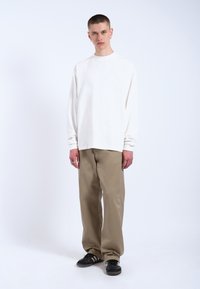 Witte overhemd met lange mouwen, relaxed fit; khaki losse broek; zwarte schoenen met witte strepen; basic ontwerp, gladde stoftextuur.