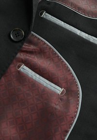 Black fabric with maroon patterned panel and gray accents. Features a button and two pockets. Stitching detail along edges.