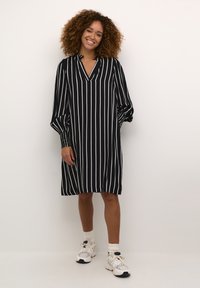 Schwarz-weiß gestreiftes Kleid mit V-Ausschnitt, langen Puffärmeln und lockerer Passform, kombiniert mit strukturierten weißen Sneakers und Socken.