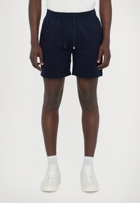 Shorts en velours côtelé bleu marine avec une taille élastique, un cordon de serrage et deux poches latérales. Texture lisse et coupe décontractée. Baskets et chaussettes blanches.