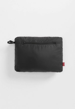 Cuscino rettangolare nero con una texture liscia, dotato di una chiusura a zip e un piccolo etichetta rossa su un lato.