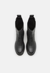 Botas de tornozelo em couro preto com um acabamento liso, painéis laterais elásticos e alças de puxar. Bico redondo e sola de borracha para maior aderência.