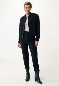 Svart bomberjacka över en grå topp, matchad med skräddarsydda svarta byxor och gröna klackiga ankelstövlar. Har knappstängning och fickor.