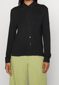 Svart långärmad skjorta med krage, framknäppning och mjuk textur. Matchas med ljusgröna byxor som har en lös passform.
